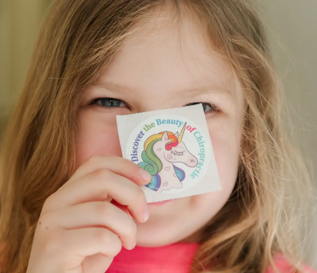 Young girl smiling with a cute kid's chiropractic sticker after receiving chiropractic care for kids and teens in London Ontario.