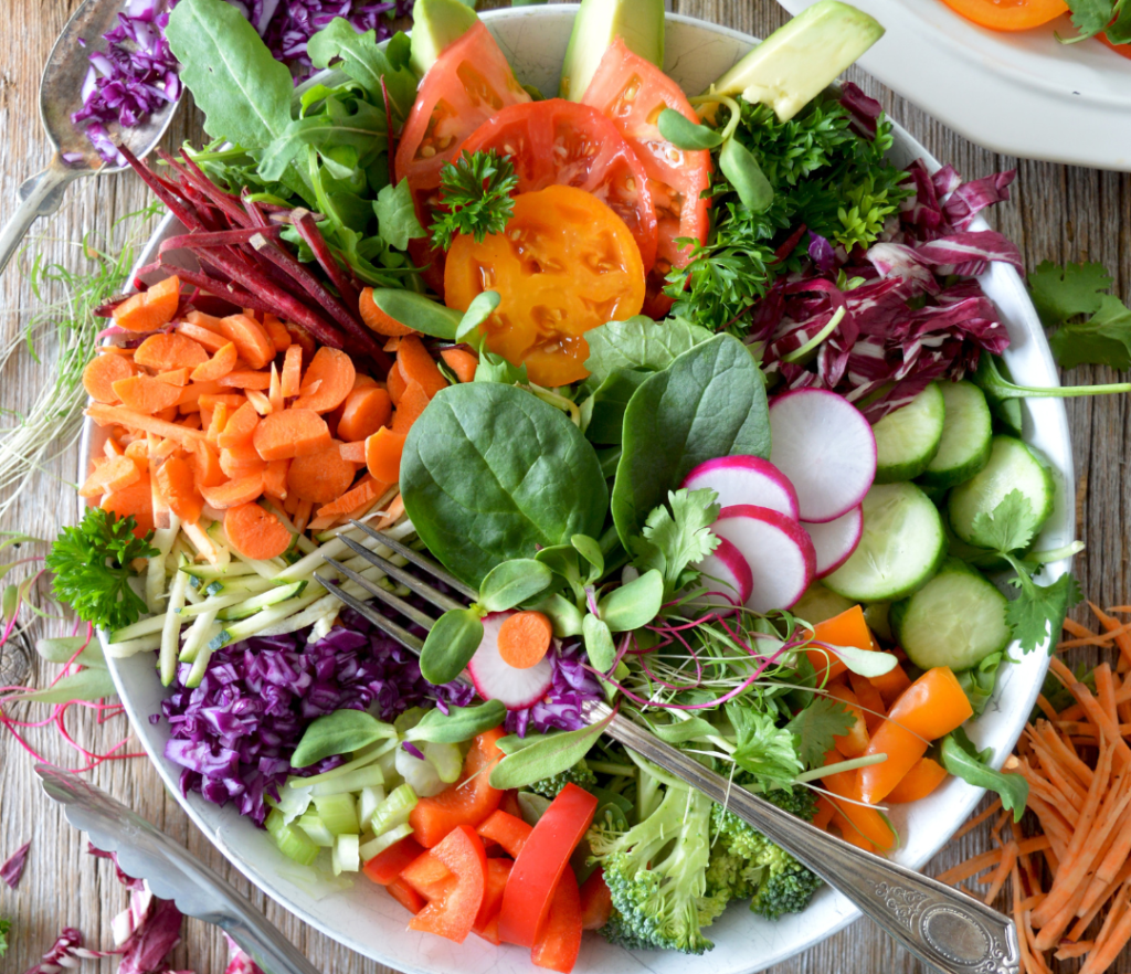 A bowl of fresh vegetables to inspire ways to eat more veggies, including carrots, bell peppers, cucumbers, and leafy greens.