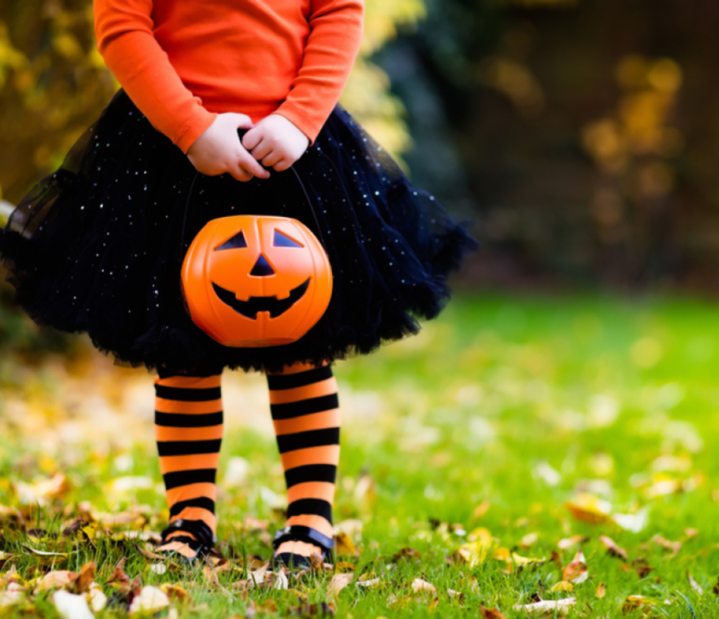 A child dressed as a witch in striped stockings carrying a Halloween pail ready to have fun while following some healthy Halloween tips from Dr. Janna.