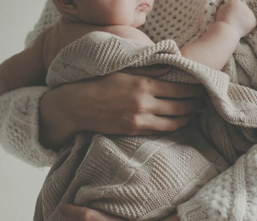 Postpartum chiropractic care in London Ontario - Arms of a mother holding a newborn baby wrapped in a cozy blanket.